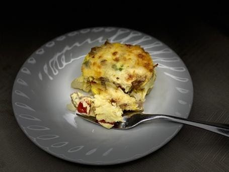 A slice of savory quiche with visible layers of vegetables and a golden-brown top resting on an elegant white plate, partially eaten with a fork alongside.