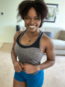 A joyful woman in workout gear posing with a bright smile in a home interior.