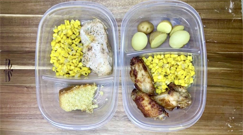 Meal prep containers with a well-balanced meal, including grilled chicken breast, corn, baby potatoes, and a piece of cornbread.