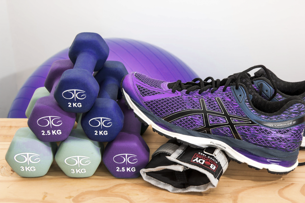 A collection of workout equipment featuring a set of colorful dumbbells, an exercise ball, and a pair of purple athletic shoes, suggesting preparation for a fitness session.