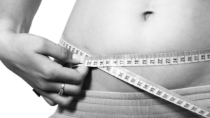 Close-up of a person measuring their waist with a tape measure, focusing on health and fitness.