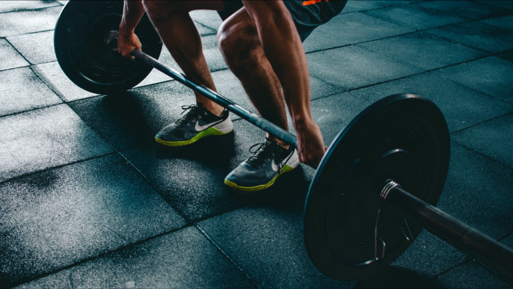 A weightlifter preparing to execute a deadlift, focusing on the grounded barbell and their powerful stance.