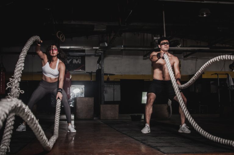 Intensity and focus: a man and woman engaging in a dynamic battle rope workout at the gym.