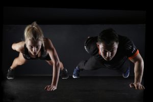 Two athletes performing push-ups with determination and focus in a gym setting.