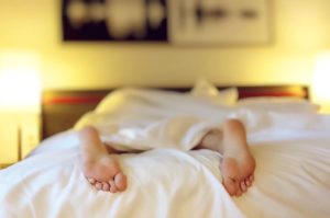 A person's feet peeking out from the end of a cozy, untidy bed, suggesting a relaxed or lazy morning.