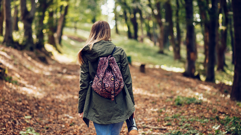 A woman with a patterned backpack wandering through a sun-dappled forest, immersed in the tranquility of nature.