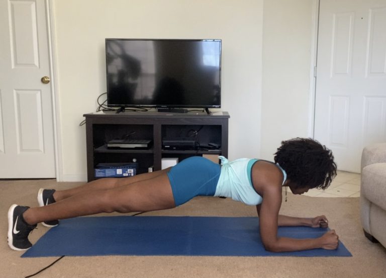 A person practicing a forearm plank exercise on a blue mat in a living room, maintaining fitness at home.