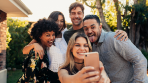 Group of joyful friends taking a selfie outdoors with wide smiles.