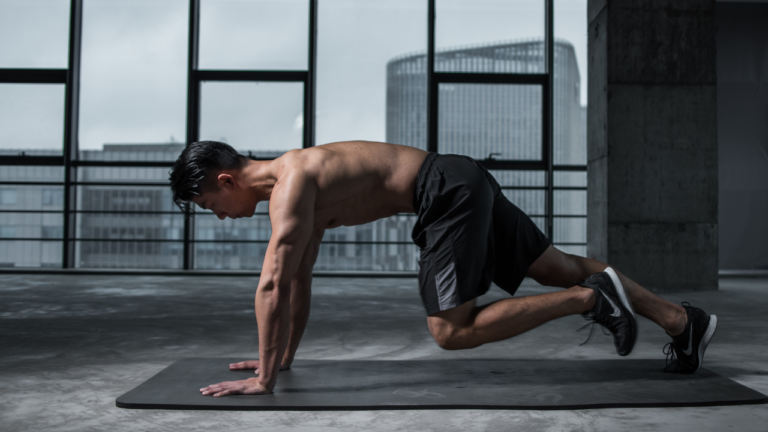 A man demonstrating strength and focus as he performs a one-armed push-up on a yoga mat in an urban, industrial-style setting with large windows.