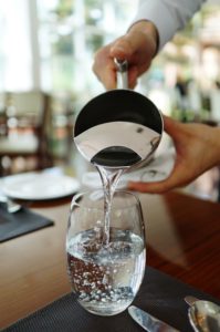 Pouring fresh water into a glass at a dining table.