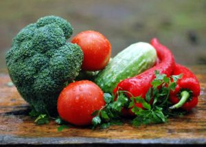 A vibrant array of fresh vegetables, including broccoli, tomatoes, cucumber, red bell peppers, and garnished with parsley, on a rustic wooden surface with droplets of water suggesting freshness.