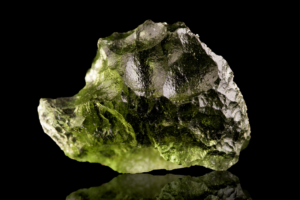 A translucent green gemstone with rough facets glistening, showcased against a dark background.
