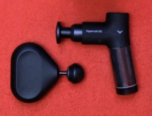 Portable black massage gun with attachments on a red background.