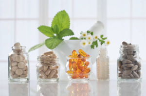 Assorted dietary supplements in glass jars with a backdrop of fresh herbs and flowers, suggesting a theme of natural health and wellness.