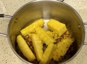 Fresh pineapple chunks and core pieces in a stainless steel pot, possibly ready for cooking or making pineapple juice.
