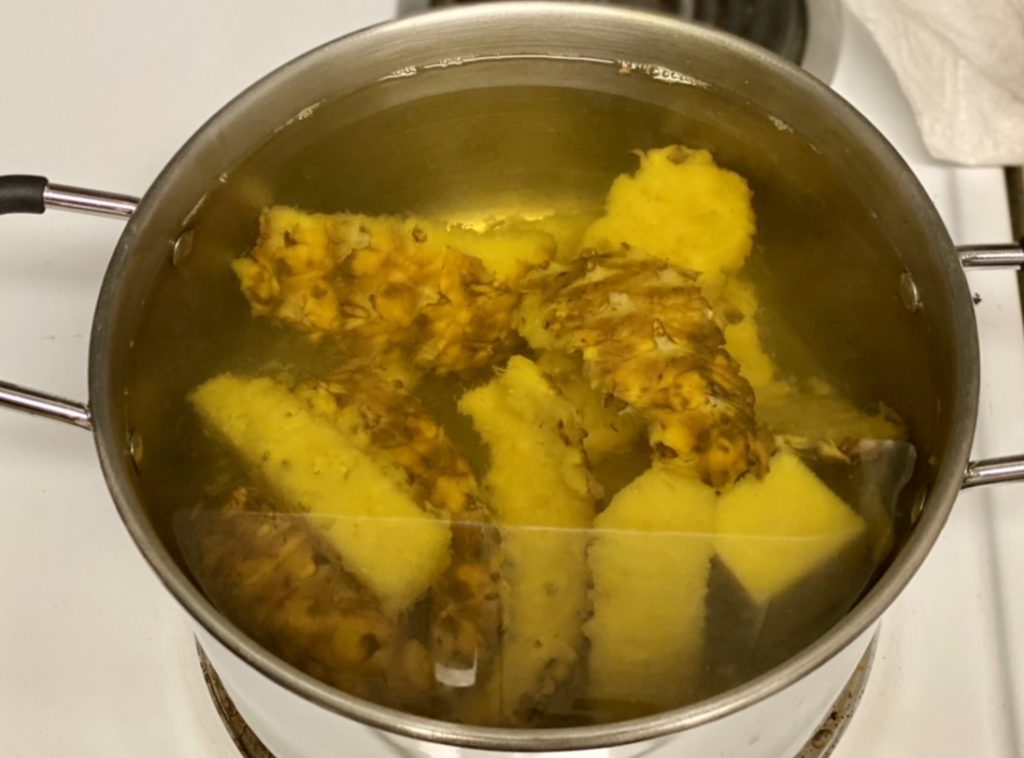 Sliced pineapples boiling in a stainless steel pot on a stove.