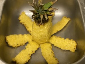 A pineapple creatively cut and cored with its outer skin sliced off and spread out to resemble a star, placed in a metal kitchen sink.