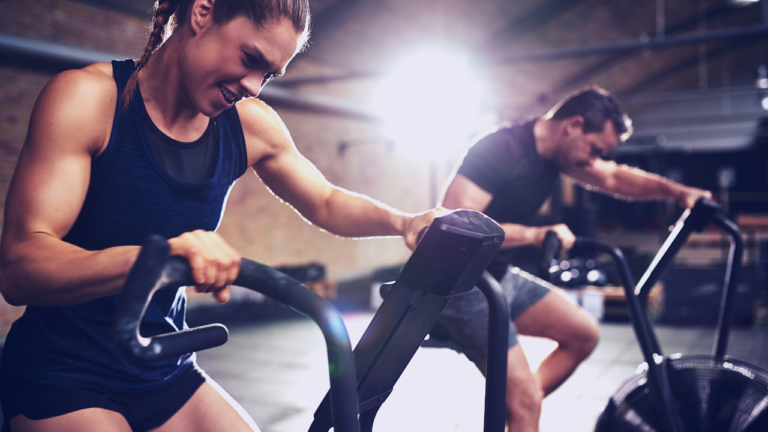 Intense indoor cycling session: a focused woman and man pushing their limits on stationary bikes in a gym setting.