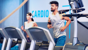 Two individuals focused on their cardio workouts, running on treadmills in a modern gym setting.