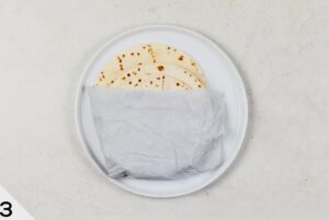 A plate with several queso fondue steak quesadillas partially wrapped in a paper towel.