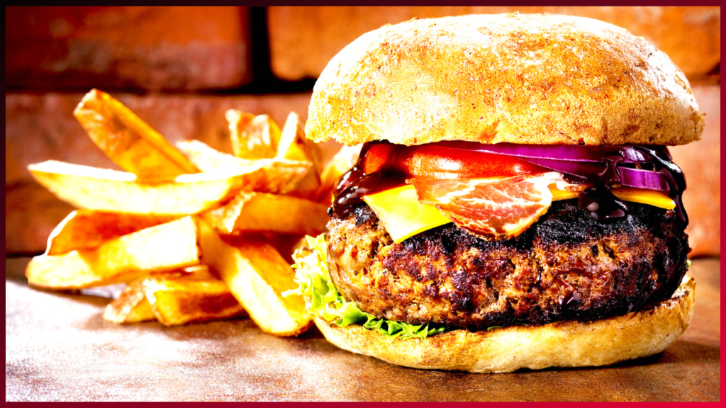 A juicy gourmet burger topped with melted cheese, crisp bacon, and fresh vegetables, accompanied by a side of golden-brown french fries, presented tantalizingly on a rustic table.