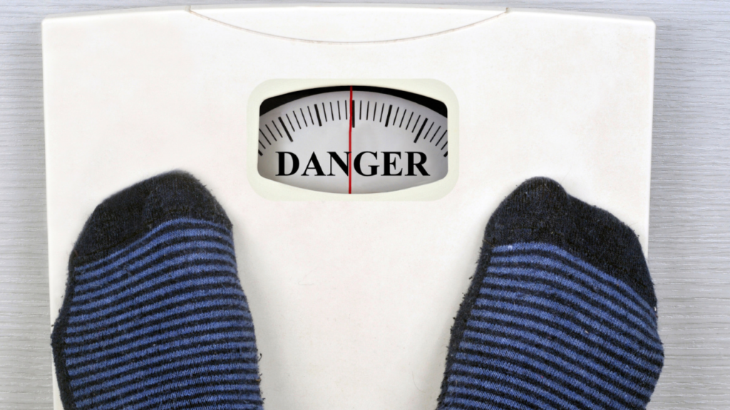 Feet standing on a weighing scale with the dial indicating "danger" - a conceptual image of health risk due to weight issues.