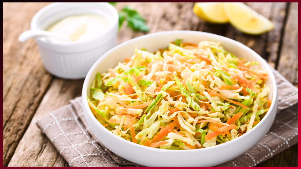 A fresh bowl of coleslaw salad with shredded cabbage and carrots, served on a wooden table with a side of creamy dressing and slices of lemon.