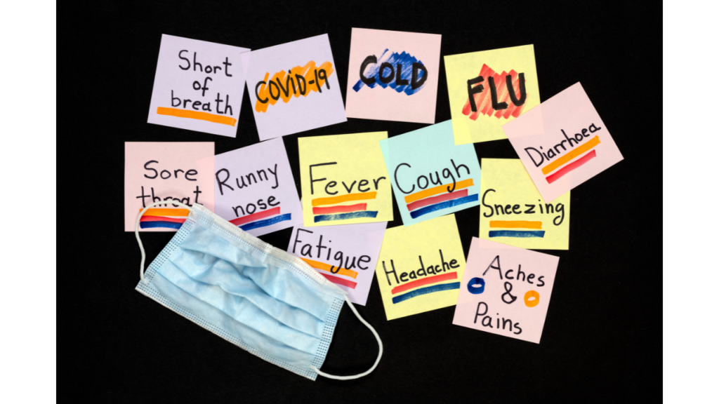 Colorful sticky notes with common illness symptoms written on them, such as "fever," "cough," "sneezing," surround a blue surgical mask on a black background.