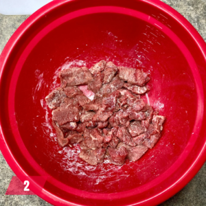 Raw beef pieces in a red mixing bowl, ready for marinating or cooking for a Mongolian Beef recipe.