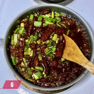 A savory and glossy Mongolian Beef recipe with chunks of meat and green onions, simmering in a rich, dark sauce in a skillet, accompanied by a wooden cooking spoon.