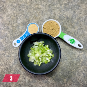 Prepping spices and chopped green onions for a Mongolian Beef recipe, with measuring spoons of garlic and ginger powder on a kitchen counter.