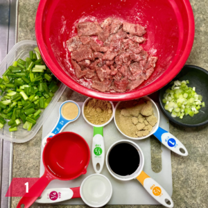 Ingredients prepared for a Mongolian Beef recipe: diced green onions, sliced scallions, marinated beef in a red bowl, and various spices and seasonings measured out, ready for cooking.
