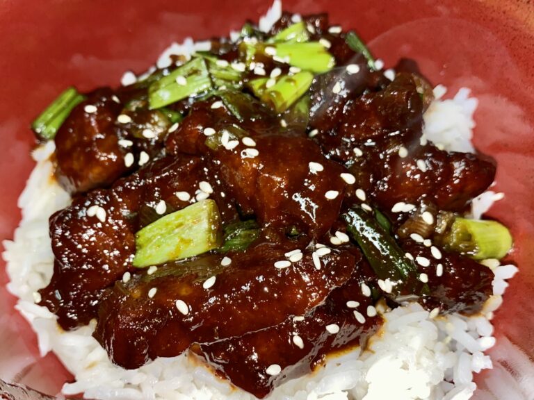 Savory and glossy Mongolian Beef served over a bed of steamed rice, garnished with green onion and sprinkled with sesame seeds.
