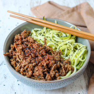 A bowl of 15 Plant-Based Recipes - eBook noodles topped with savory minced meat and garnished with black sesame seeds, accompanied by a pair of wooden chopsticks.