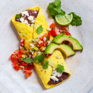 A vibrant plate featuring a folded omelet with a side of fresh tomato salsa, creamy avocado slices, and a lime wedge, garnished with cilantro Gluten-Free Recipes - eBook.