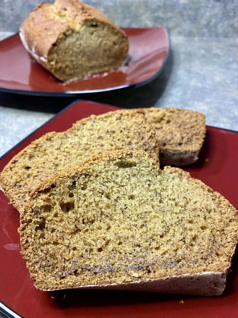 Slices of freshly baked banana bread served on a red plate, with the remaining loaf in the background, showcasing a moist crumb and golden-brown crust.