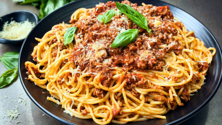 A plate of spaghetti topped with a rich meat sauce, garnished with fresh basil leaves and sprinkled with grated cheese, ready to be enjoyed.