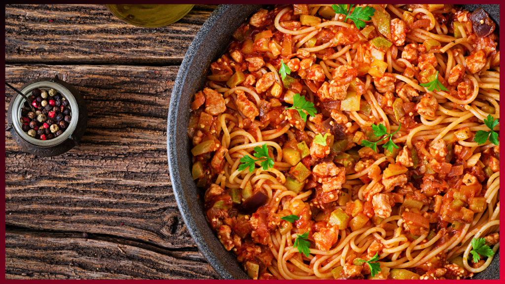 Savory spaghetti with chunky tomato sauce and herbs served in a rustic pan on a wooden table, accompanied by spices and olive oil, ready to tantalize your taste buds.