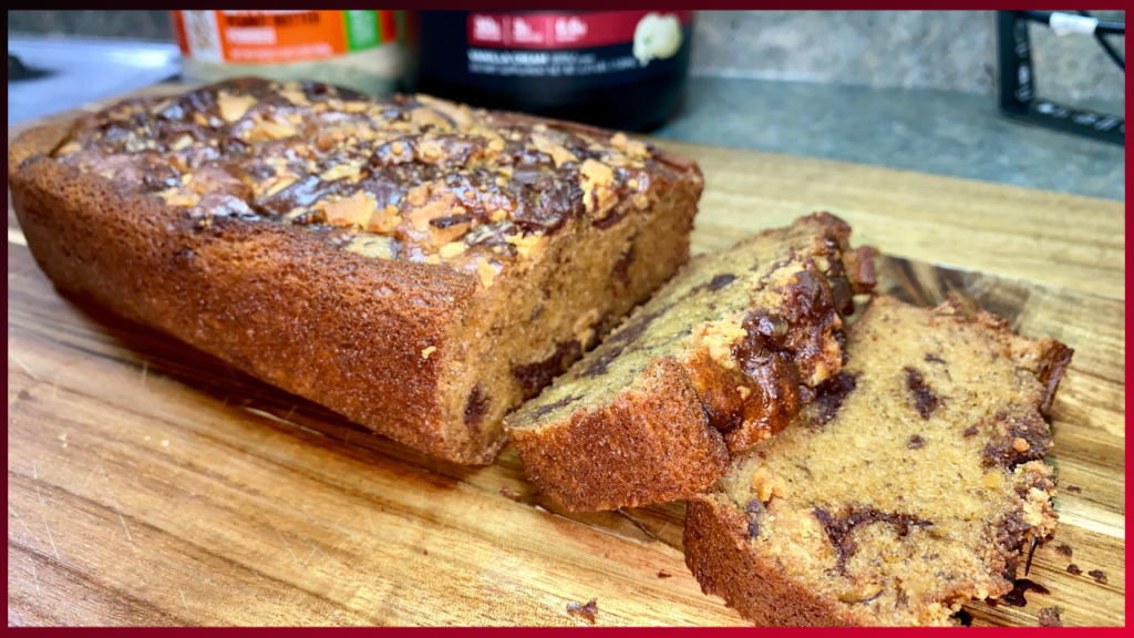 A freshly baked loaf of nut-studded banana bread on a wooden cutting board with slices ready to enjoy.
