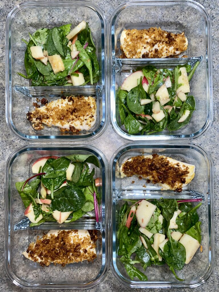 Three glass containers each filled with grilled chicken fillets and spinach salad with apple slices, divided into individual meal prep portions. The containers are arranged in two columns, showcasing the organized and healthy meal plan.