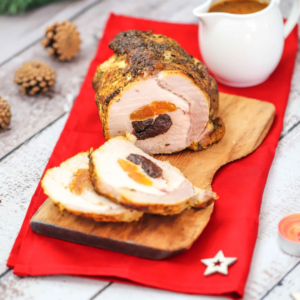 The Holiday Treats [1] eBook features a sliced rolled pork roast with apricot and prune filling, elegantly presented on a wooden board with a red cloth. In the background is a white gravy boat, with small pine cones and a star-shaped decoration completing the festive setting.