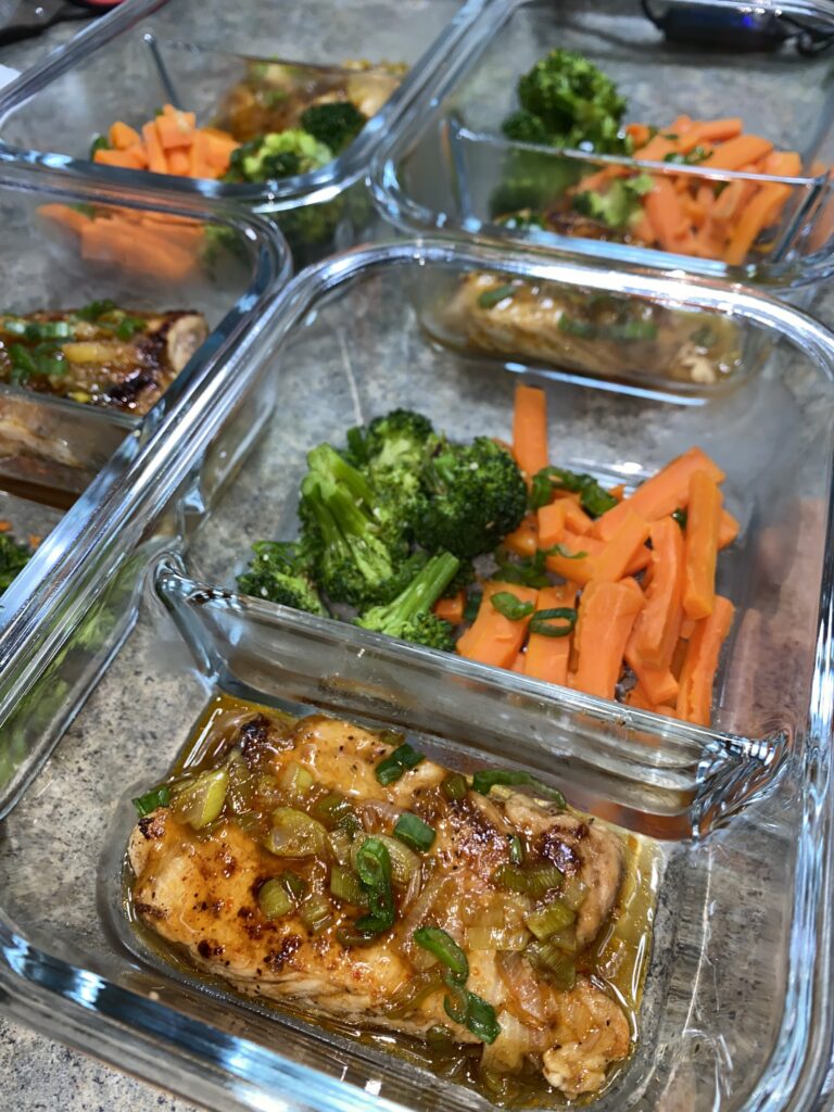 Glass containers filled with meal-prepped portions of glazed chicken, steamed broccoli, and sliced carrots, arranged on a countertop.