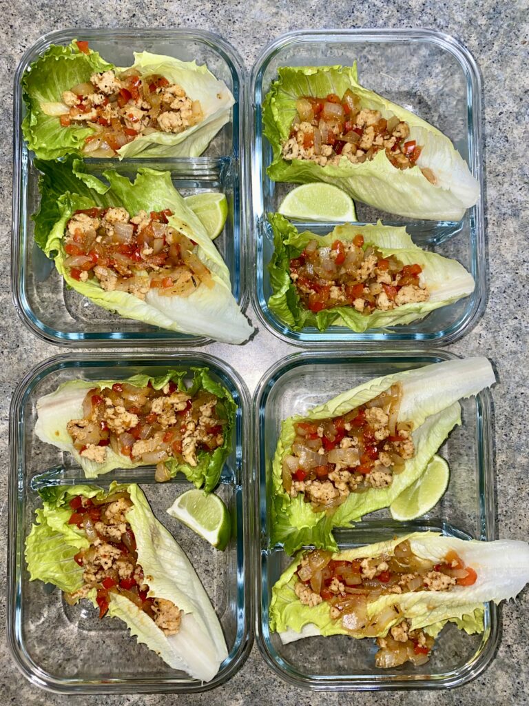 Glass containers filled with lettuce wraps, each topped with a mixture of cooked ground meat, diced vegetables, and garnished with lime wedges, arranged neatly on a speckled countertop.