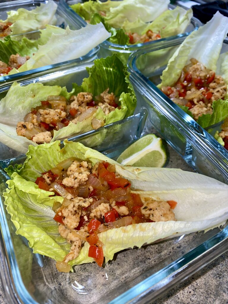 Several glass containers hold lettuce wraps filled with seasoned ground turkey, diced red bell peppers, and onions. Lime wedges are placed beside the wraps.