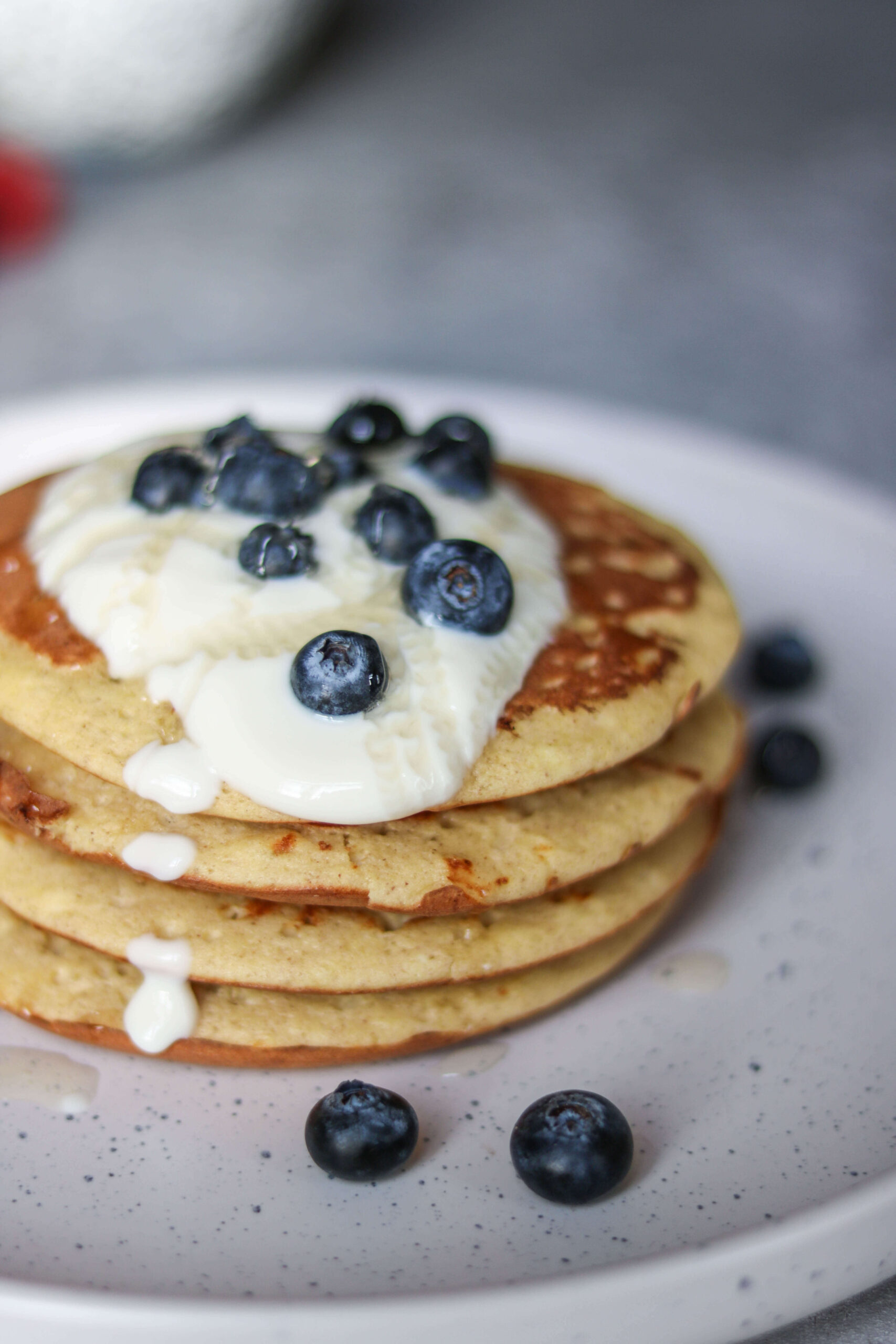 A delicious stack of pancakes from The New Year Reset Recipe Bundle, topped with creamy yogurt and fresh blueberries, served on a white plate with extra blueberries scattered around.