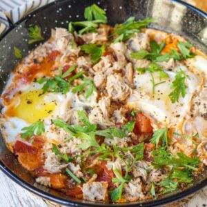 A skillet of poached eggs in tomato sauce with tuna and parsley sits by toast, featured in The New Year Reset Recipe Bundle.