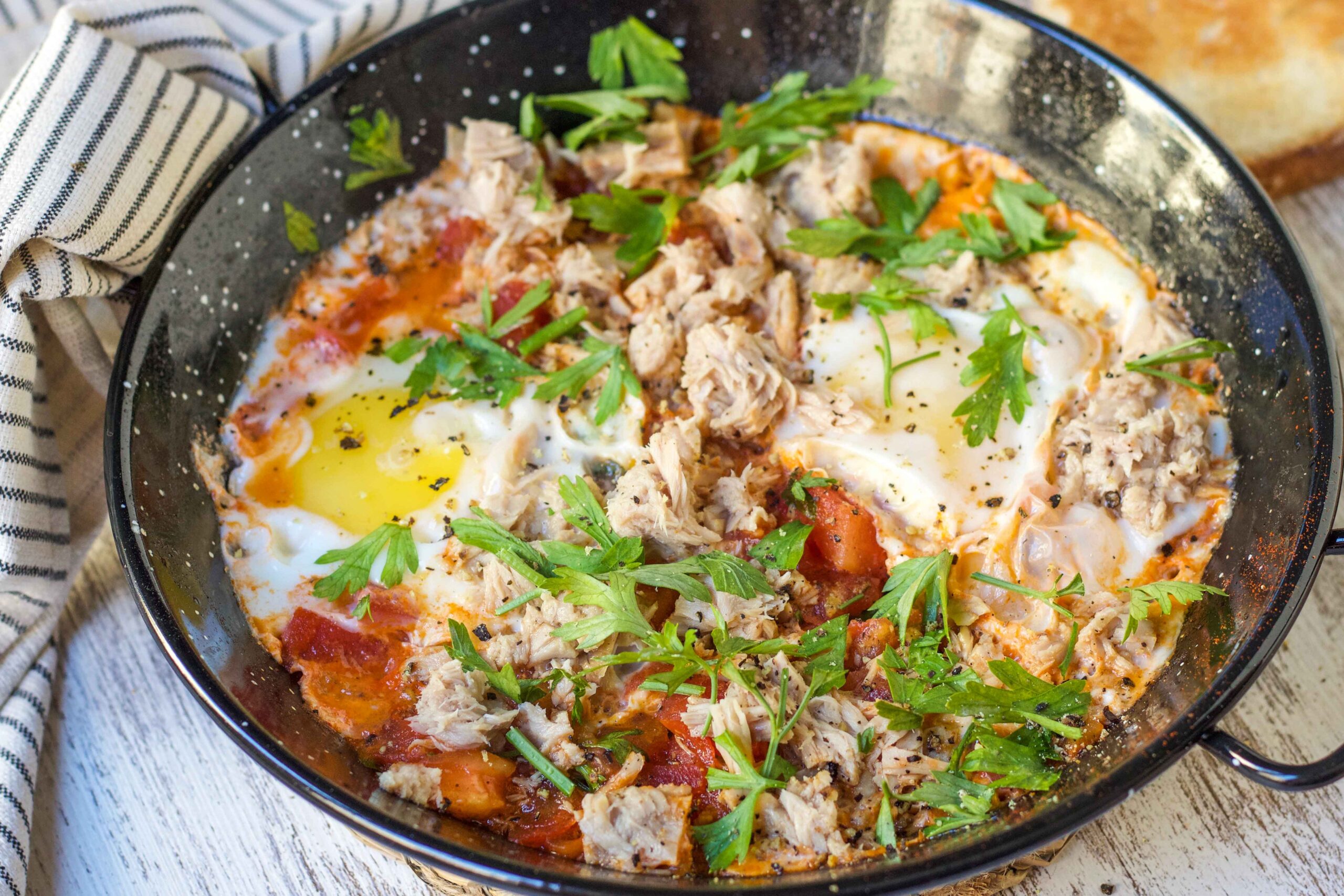 A skillet of poached eggs in tomato sauce with tuna and parsley sits by toast, featured in The New Year Reset Recipe Bundle.
